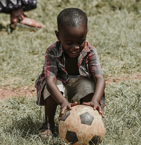 An African child kneeling over a black and white striped football
