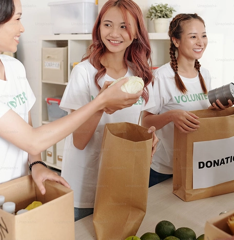 Three young volunteers in donation-drive t-shirts packaging food donations together